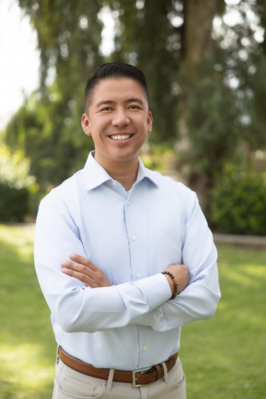 Eric Arias smiling with his arms crossed in a park